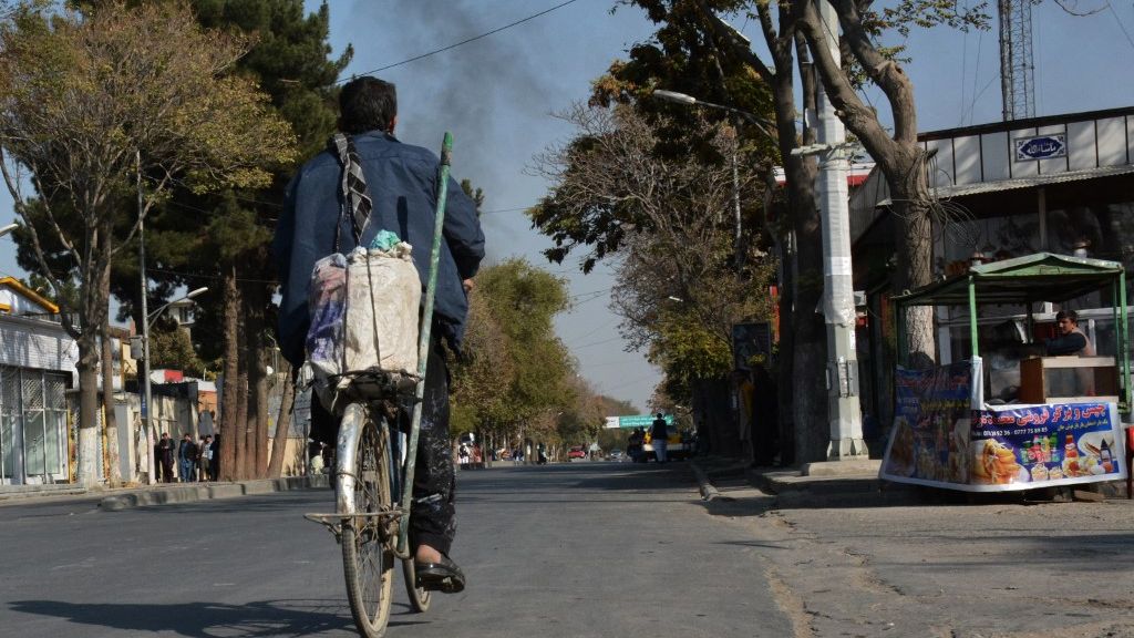 Un hombre afgano monta una bicicleta con el telón de humo al fondo / AFP